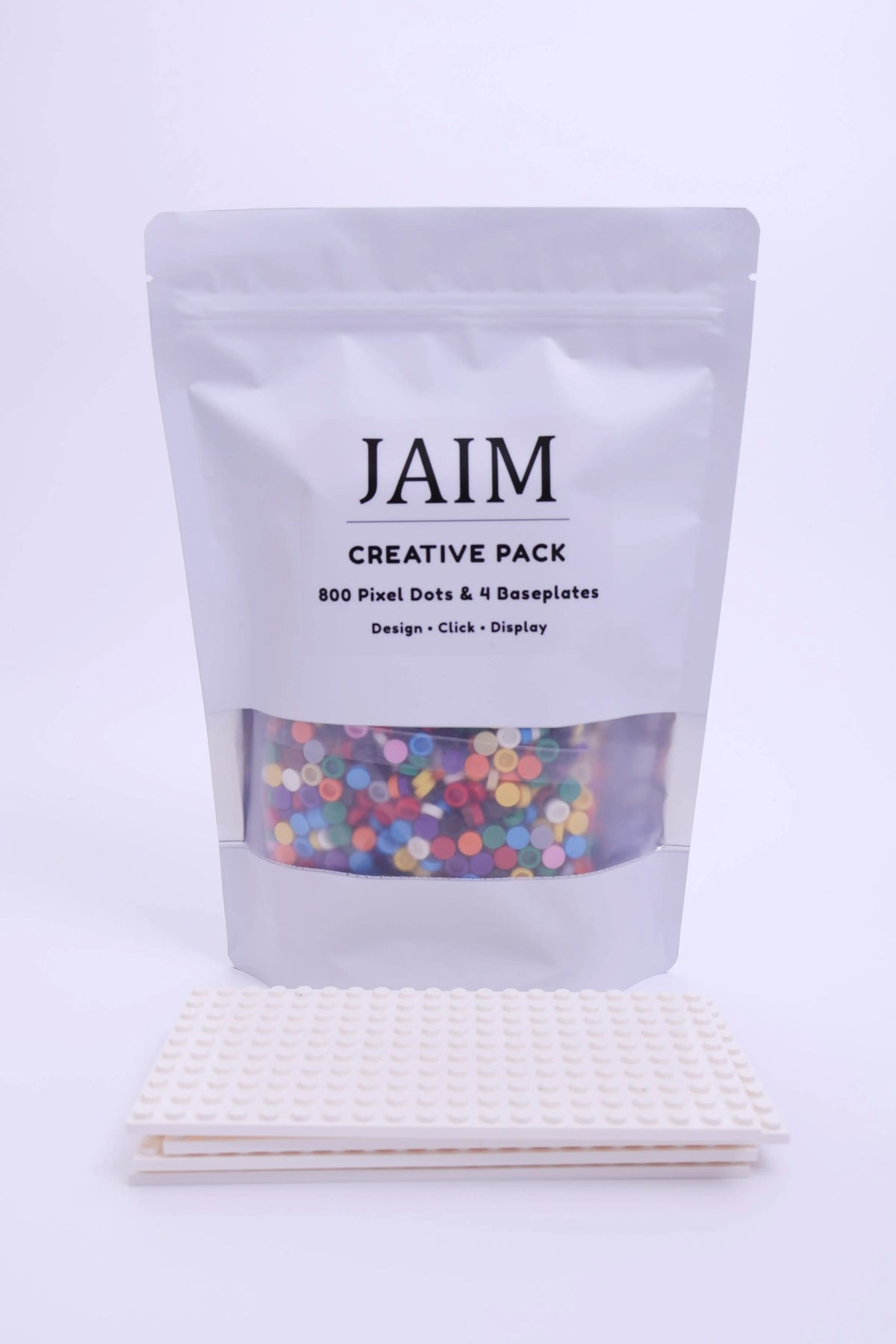 A white stand-up pouch labeled 'JAIM CREATIVE PACK' with a clear window showing multicolored pixel dots, placed above two white pixel art baseplates on a clean white background.